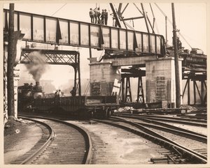 Arbeiders staand op een stellage terwijl een trein eronderdoor rijdt in een onbekend rangeerterrein door William G. Swekosky